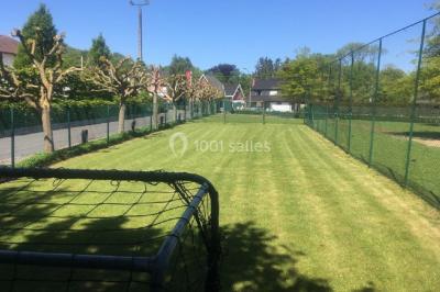 Structure de jeux en plein air avec toboggan et modules d'escalade, installée sur un sol sablonneux près d'une clôture.