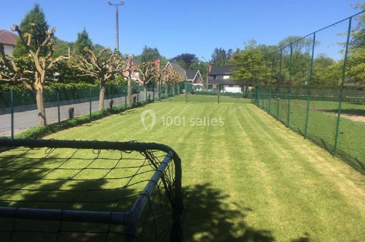 Terrain de sport en herbe entouré de clôtures, avec un but au premier plan et des arbres en arrière-plan.