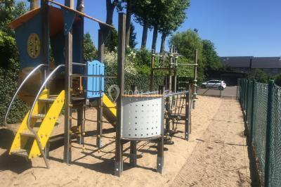 Structure de jeux en plein air avec toboggan et modules d'escalade, installée sur un sol sablonneux près d'une clôture.