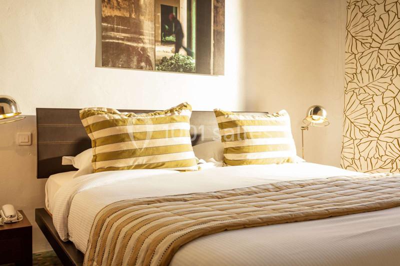 Lit double avec draps blancs, coussins rayés beige et or, éclairé par des lampes de chevet dans une chambre lumineuse.