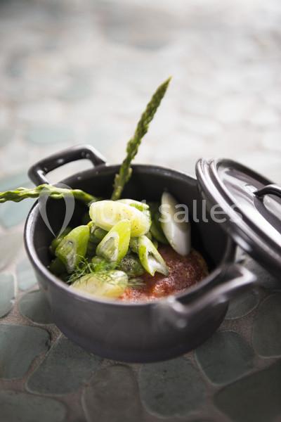 Plat dans une cocotte noire contenant un morceau de viande, des poireaux, des asperges et des herbes fraîches.
