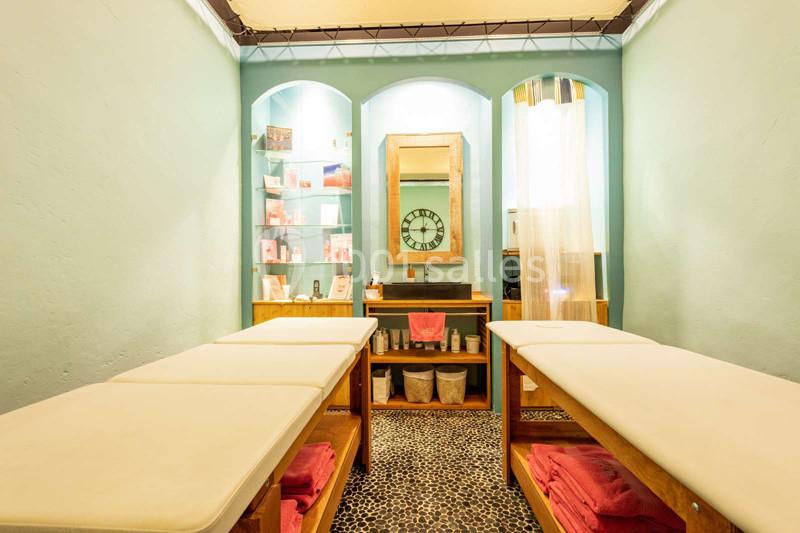 Salle de soins avec deux tables de massage, étagères de produits, miroir mural et éclairage doux.