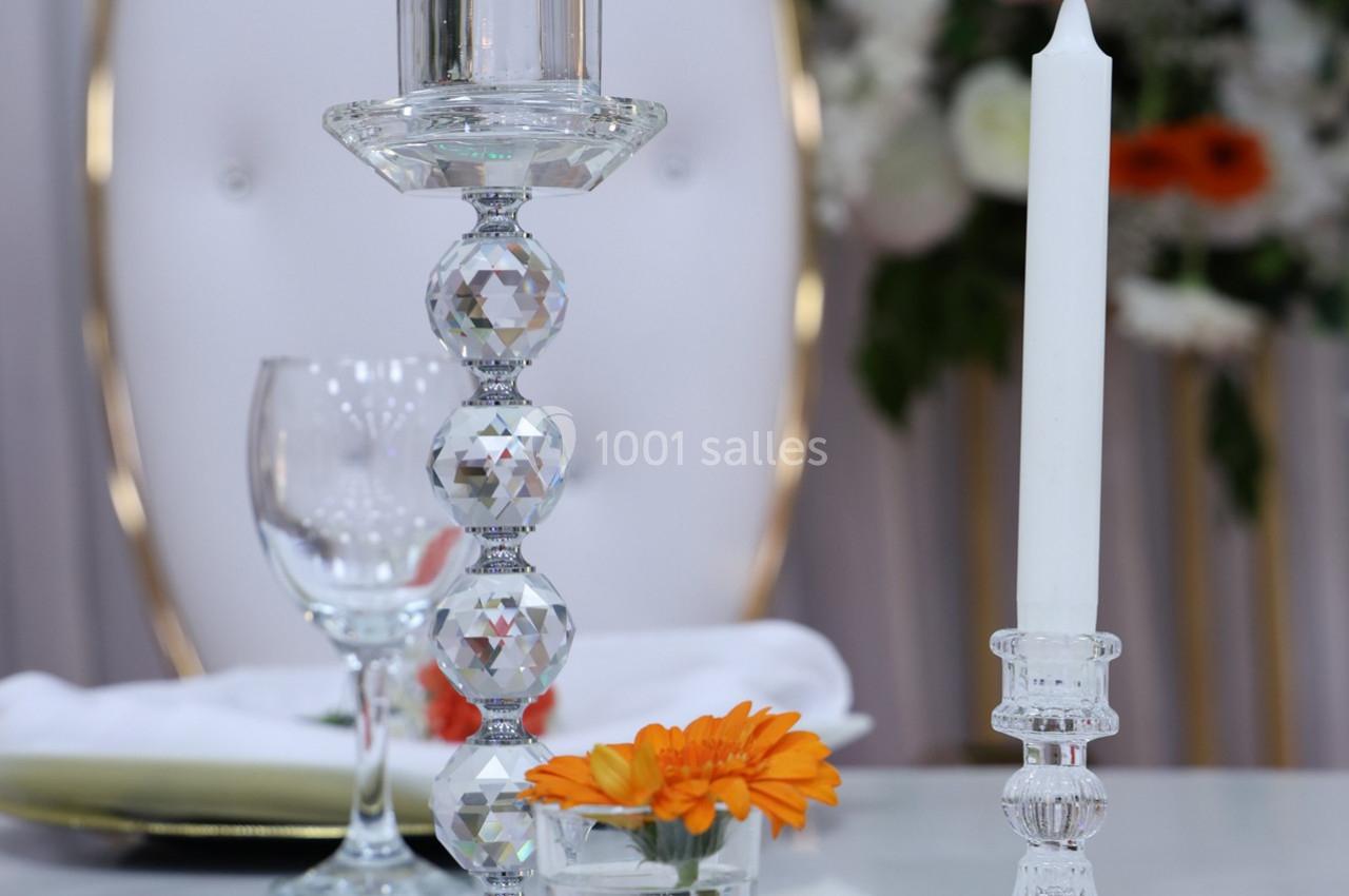 Bougeoirs en cristal avec bougies, verre à pied et fleur orange sur une table décorée, arrière-plan flou.