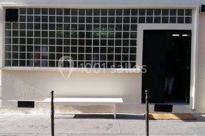 Façade d'un bâtiment avec une grande fenêtre en pavés de verre, une porte ouverte et un banc blanc devant.