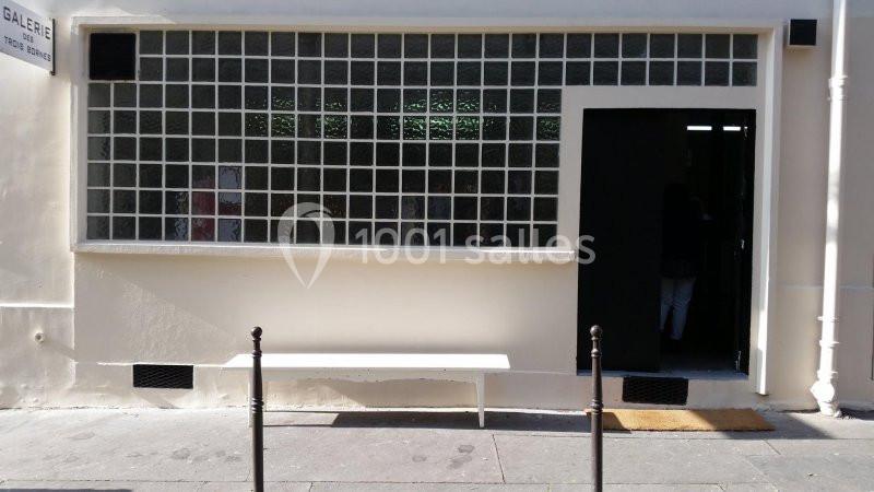 Façade d'un bâtiment avec une grande fenêtre en pavés de verre, une porte ouverte et un banc blanc devant.