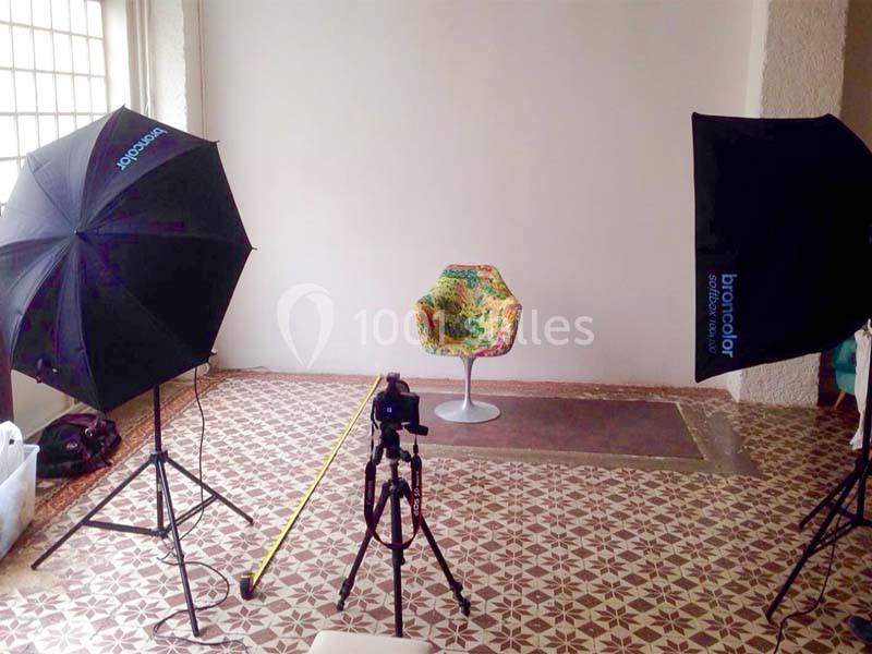 Studio photo avec une chaise colorée au centre, entourée de deux éclairages et d'un appareil photo sur trépied.