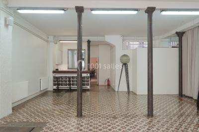 Façade d'un bâtiment avec une grande fenêtre en pavés de verre, une porte ouverte et un banc blanc devant.