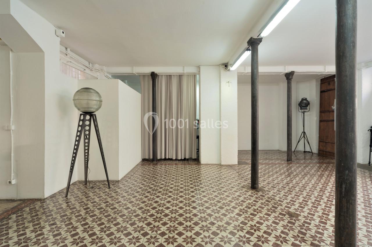 Espace intérieur avec sol en carreaux à motifs, colonnes métalliques, rideau beige et éclairage fluorescent.