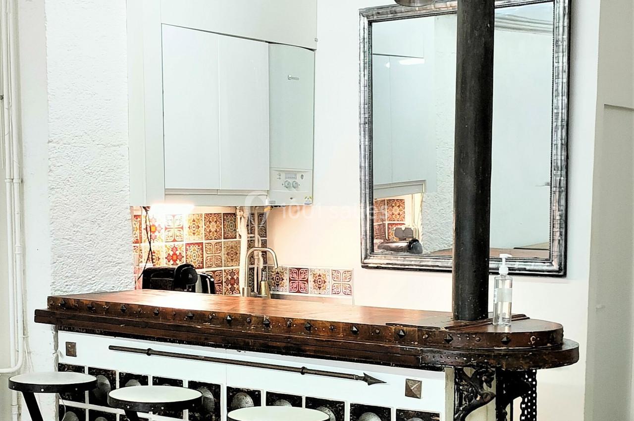 Comptoir de bar vintage avec tabourets pliants, décoré de carreaux anciens, situé dans un espace lumineux.