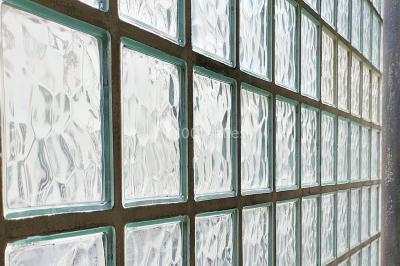 Façade d'un bâtiment avec une grande fenêtre en pavés de verre, une porte ouverte et un banc blanc devant.