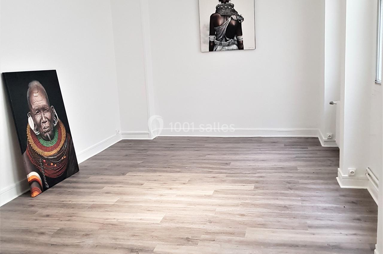 Salle vide avec parquet clair, murs blancs et deux tableaux d'art contemporain posés et accrochés.