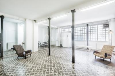 Façade d'un bâtiment avec une grande fenêtre en pavés de verre, une porte ouverte et un banc blanc devant.