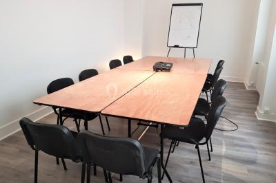 Façade d'un bâtiment avec une grande fenêtre en pavés de verre, une porte ouverte et un banc blanc devant.