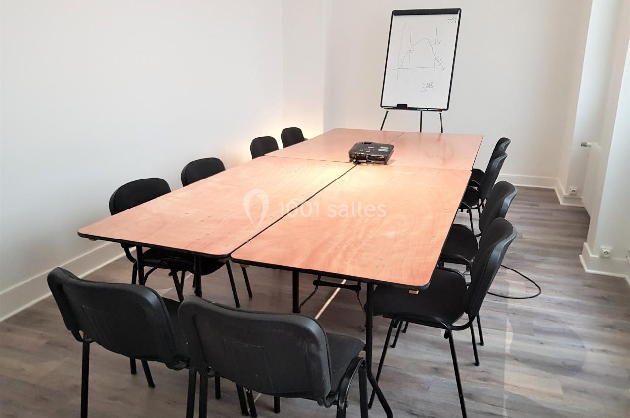 Salle de réunion avec une grande table en bois, des chaises noires et un tableau de présentation sur pied.