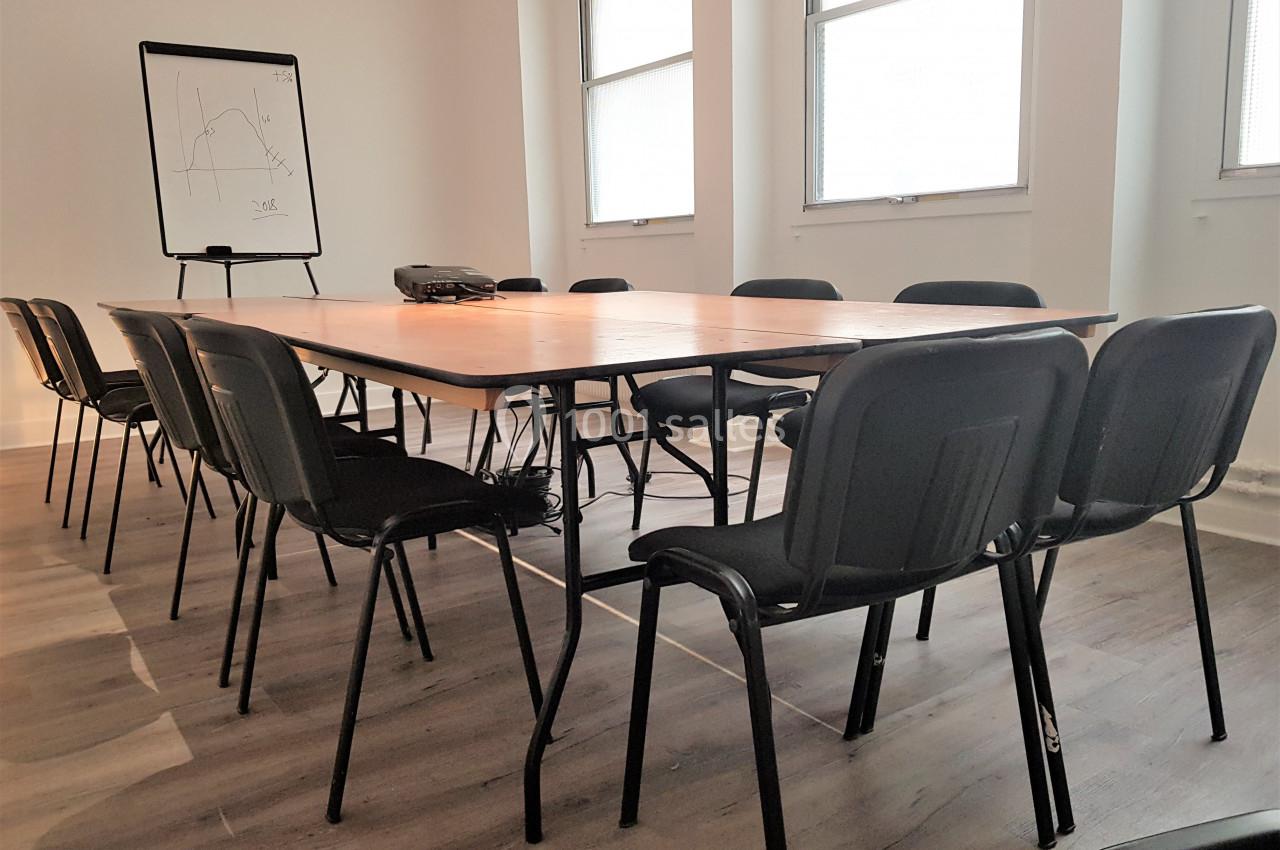 Salle de réunion avec une grande table en bois entourée de chaises noires, un tableau blanc et un projecteur.