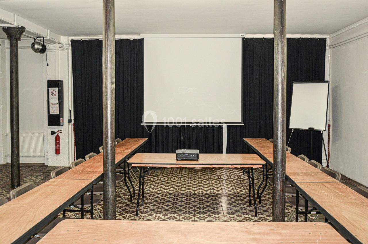 Salle de réunion avec tables en U, vidéoprojecteur, écran blanc et tableau de présentation.