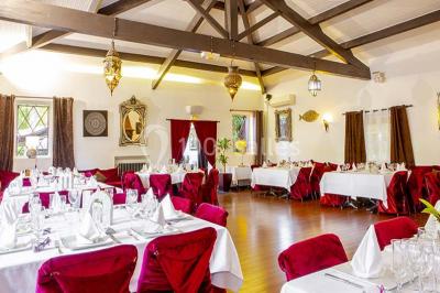 Miroir orné de motifs dorés reflétant une salle de restaurant avec cheminée, tables dressées et chaises rouges.