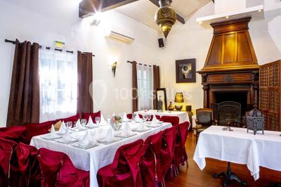 Miroir orné de motifs dorés reflétant une salle de restaurant avec cheminée, tables dressées et chaises rouges.