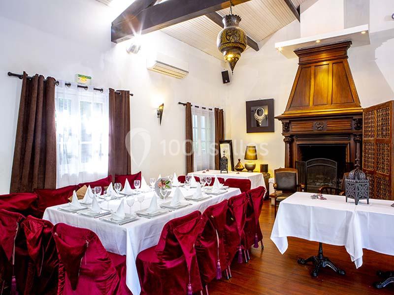 Salle à manger élégante avec tables dressées, nappes blanches, chaises rouges et cheminée en bois sombre.