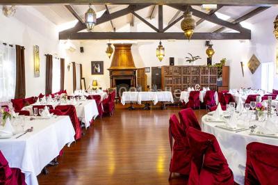Miroir orné de motifs dorés reflétant une salle de restaurant avec cheminée, tables dressées et chaises rouges.