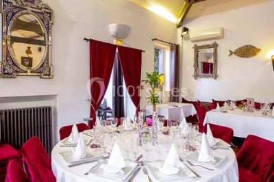 Miroir orné de motifs dorés reflétant une salle de restaurant avec cheminée, tables dressées et chaises rouges.