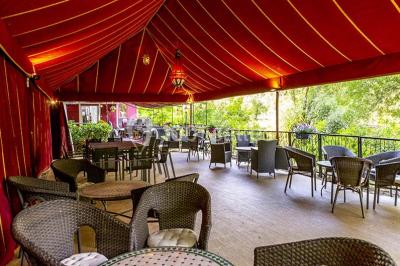 Miroir orné de motifs dorés reflétant une salle de restaurant avec cheminée, tables dressées et chaises rouges.