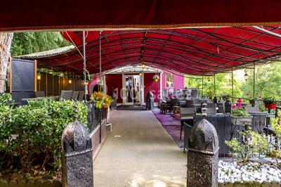 Miroir orné de motifs dorés reflétant une salle de restaurant avec cheminée, tables dressées et chaises rouges.