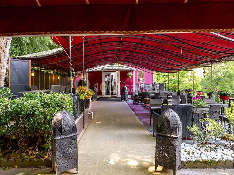 Terrasse extérieure couverte avec des tables, des chaises, des plantes et une allée centrale bordée de lanternes décoratives.