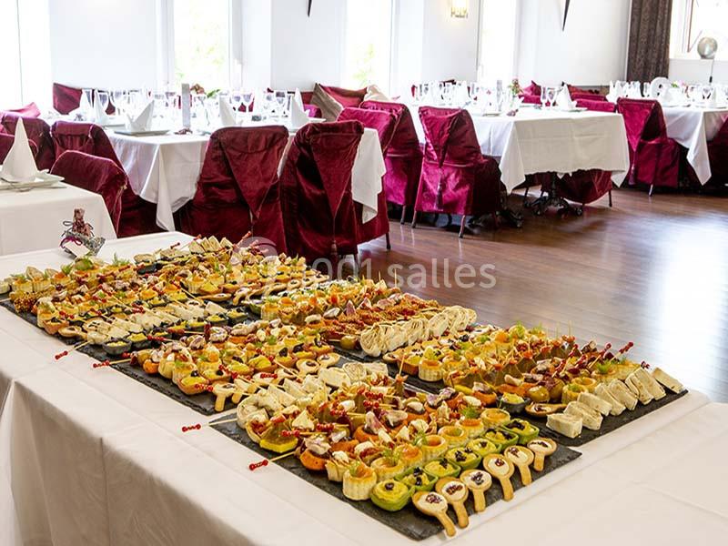 Buffet de canapés variés disposés sur une table dans une salle de réception élégante avec nappes blanches et chaises rouges.