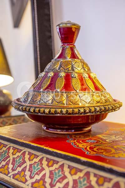 Plat à tajine décoratif rouge et doré, posé sur une table ornée de motifs colorés.
