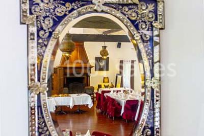Miroir orné de motifs dorés reflétant une salle de restaurant avec cheminée, tables dressées et chaises rouges.