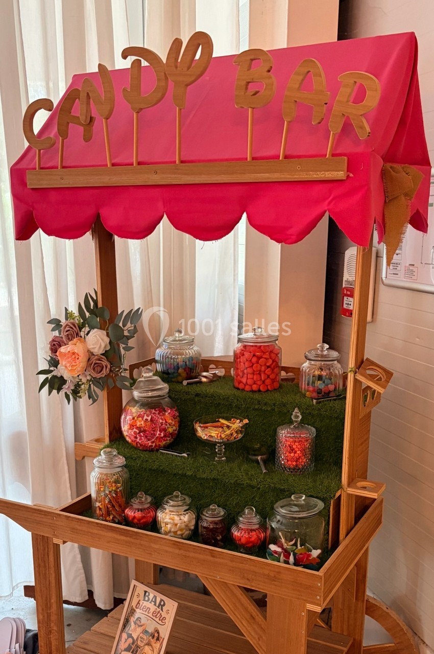 Chariot en bois décoré avec des bocaux de bonbons colorés sous une enseigne ’Candy Bar’ rose et dorée.