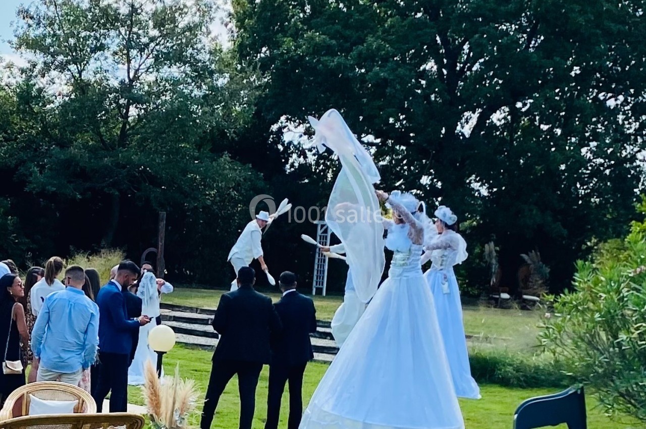 Des artistes sur échasses en costumes blancs performants dans un jardin devant un groupe de spectateurs.