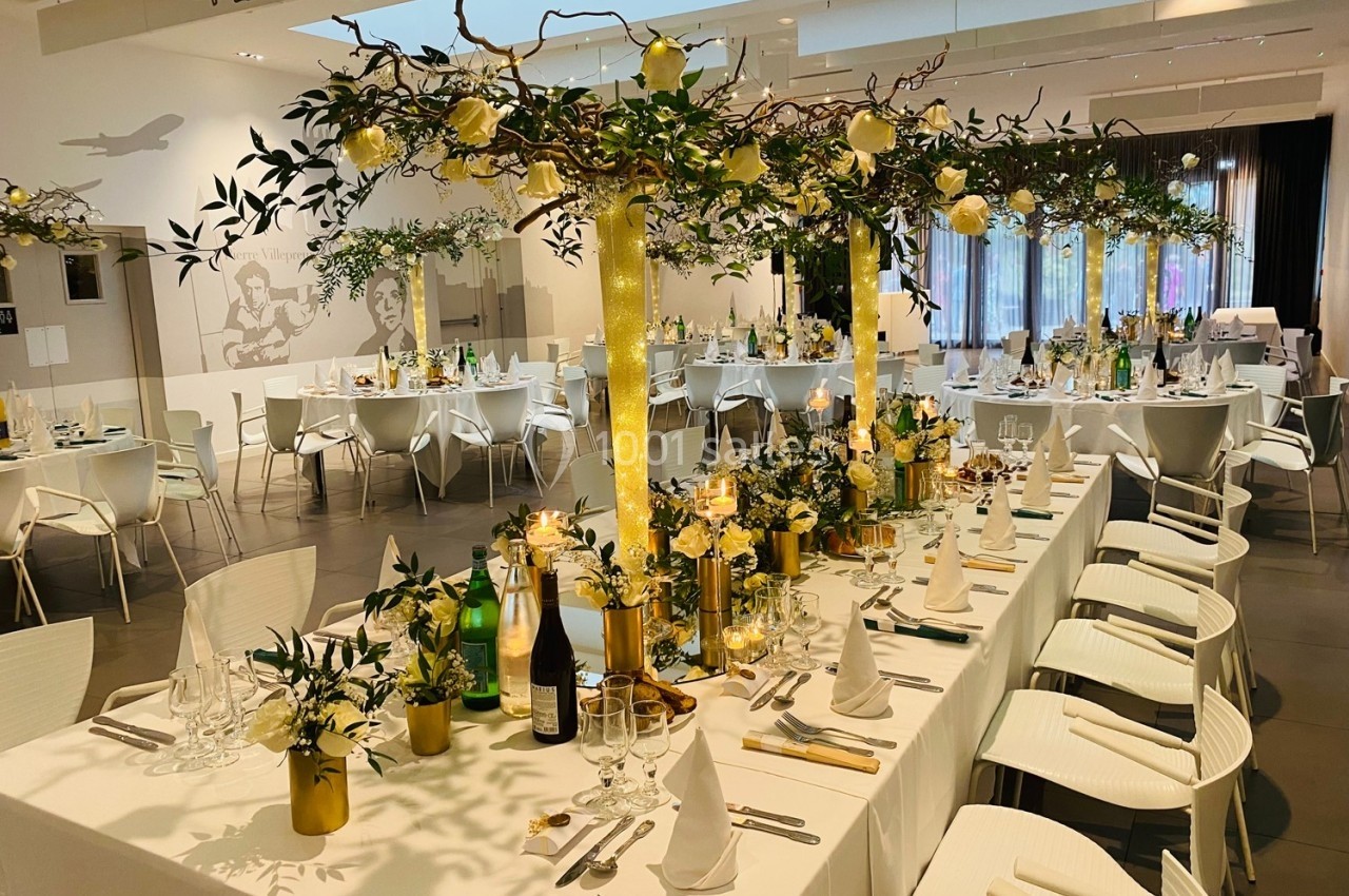 Salle de réception décorée avec des tables élégantes, ornées de fleurs jaunes et de branches suspendues.