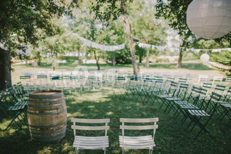 Location salle Piolenc (Vaucluse) - Château Beauchêne #5 Chaises disposées en cercle sur une pelouse, entourées d'arbres, avec une barrique et des guirlandes décoratives.