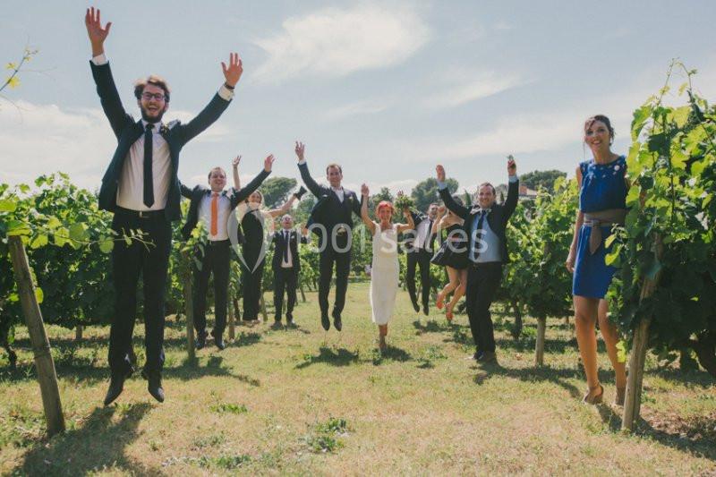 Location salle Piolenc (Vaucluse) - Château Beauchêne #7 Des personnes en tenue élégante sautent joyeusement dans un vignoble par une journée ensoleillée.