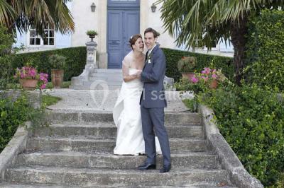 Miniature Location salle Piolenc (Vaucluse) - Château Beauchêne #17 Un couple en tenue de mariage sourit sur les marches d'un escalier en pierre devant une maison entourée de végétation.