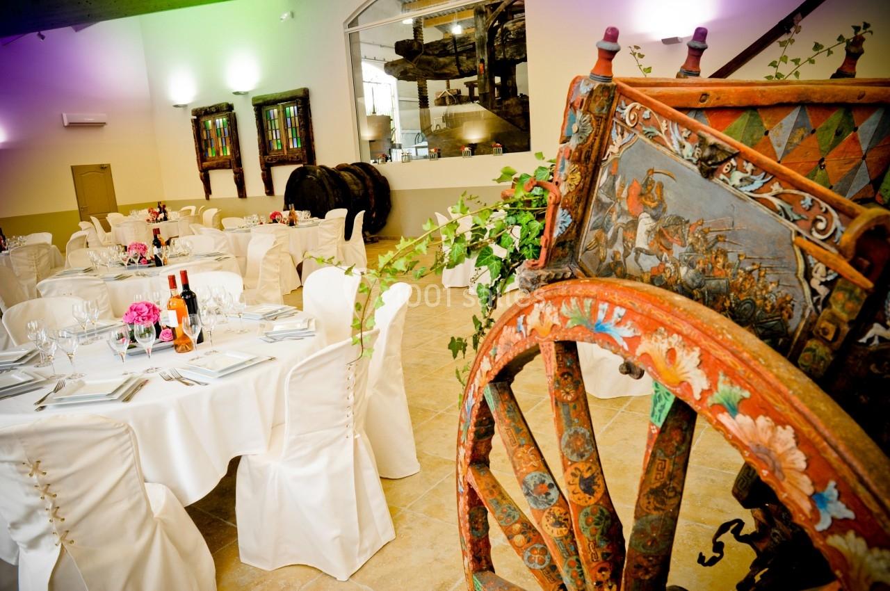 Salle de réception décorée avec des tables dressées, des tonneaux en arrière-plan et une charrette peinte au premier plan.