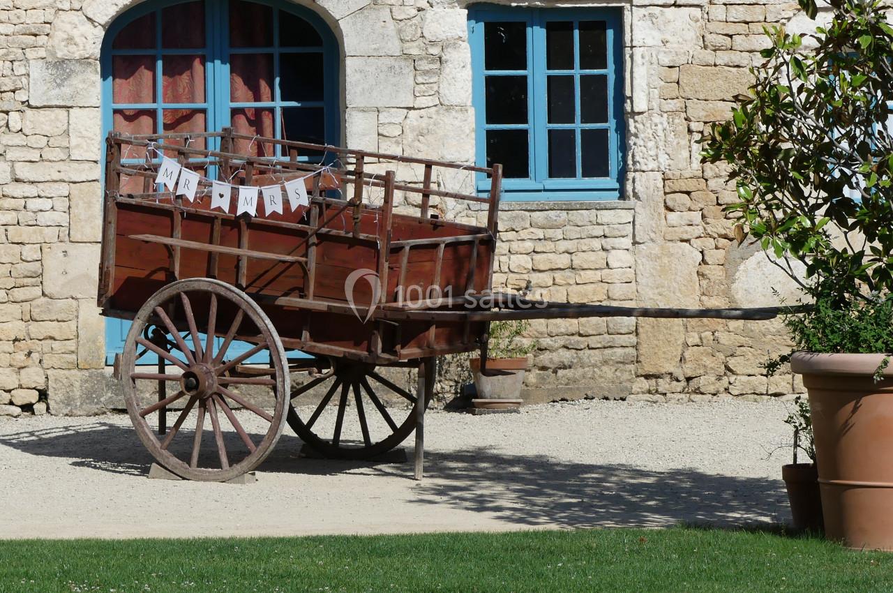 Charrette en bois ancienne avec des roues en métal, décorée d'une guirlande, devant un bâtiment en pierre.