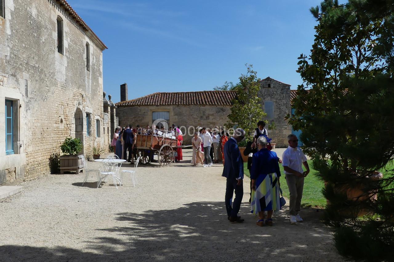 Groupe de personnes discutant dans une cour ensoleillée entourée de bâtiments en pierre et d'arbres.