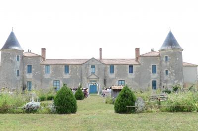 Un couple marche dans le jardin d'un château ancien entouré de verdure par une journée ensoleillée.