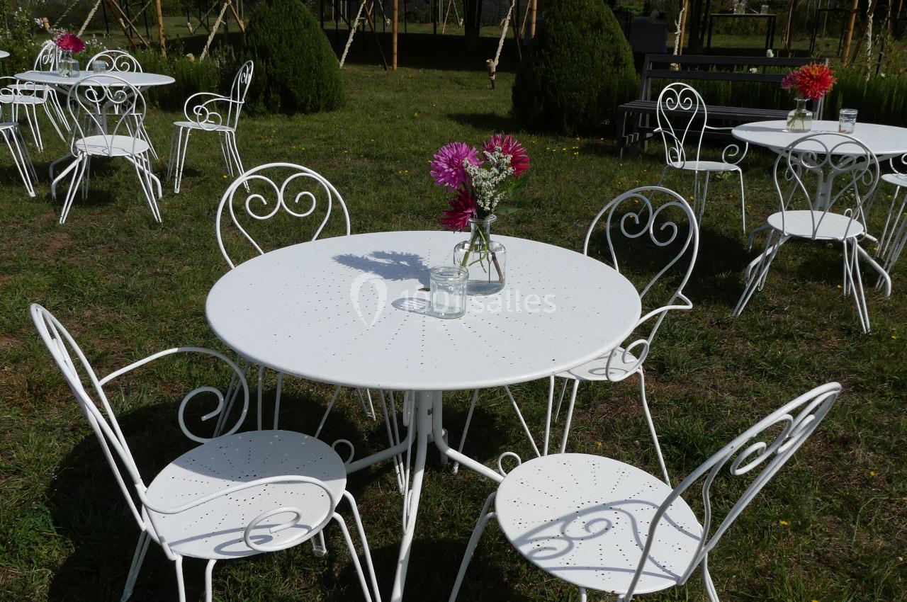 Tables et chaises en fer forgé blanc disposées sur une pelouse, avec des bouquets de fleurs au centre des tables.