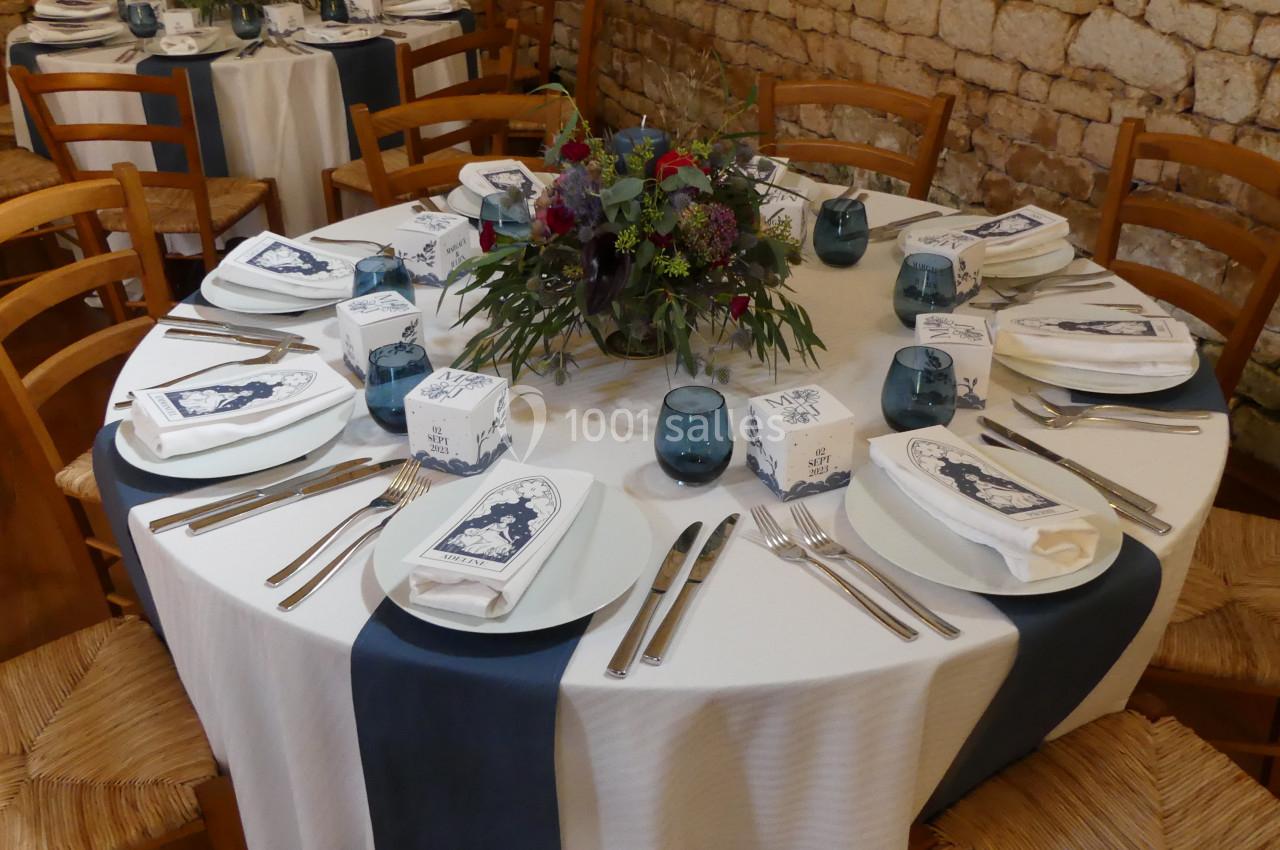 Table dressée avec nappes blanches et chemins de table bleus, ornée d'un centre de table floral et de couverts disposés.