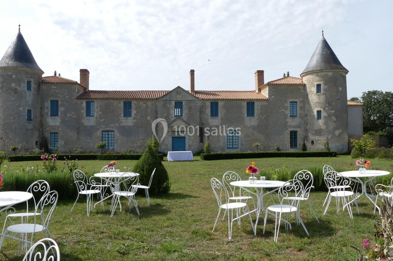 Façade d'un château ancien avec deux tours, entouré de tables blanches et d'un jardin fleuri.