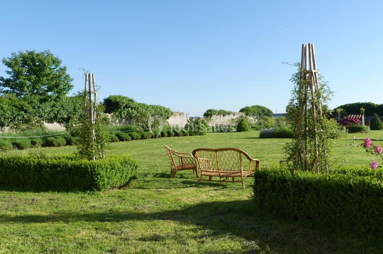 Mobilier en rotin disposé dans un jardin verdoyant entouré de haies et de structures végétales.