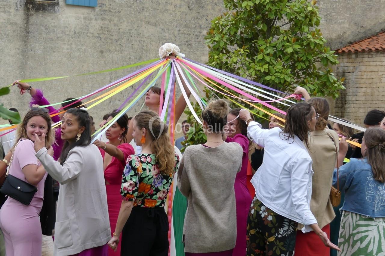 Un groupe de personnes danse autour d'un mât décoré de rubans colorés dans un espace extérieur.