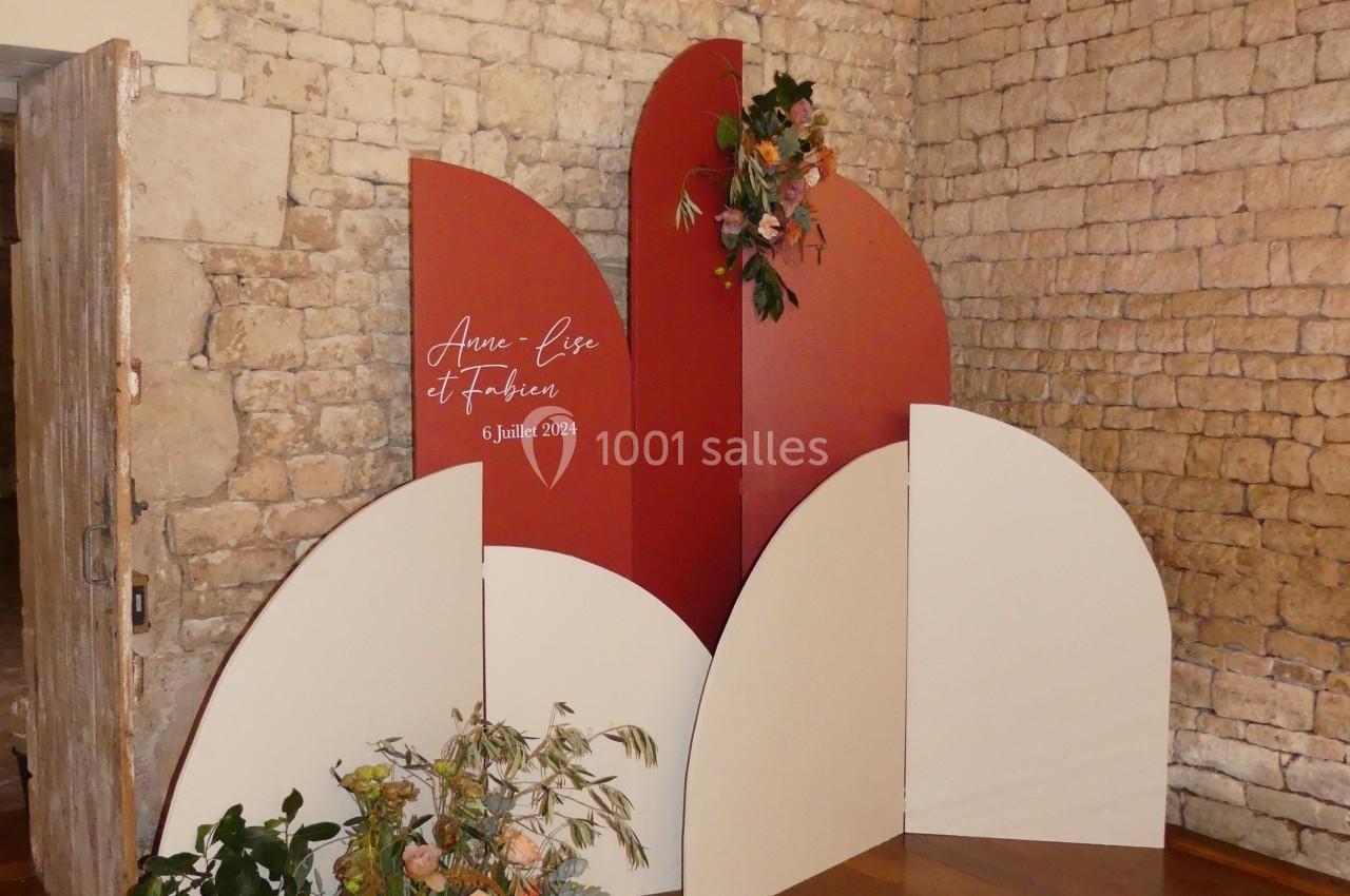 Mur décoratif en panneaux rouges et blancs avec des fleurs, installé dans une pièce aux murs en pierre.