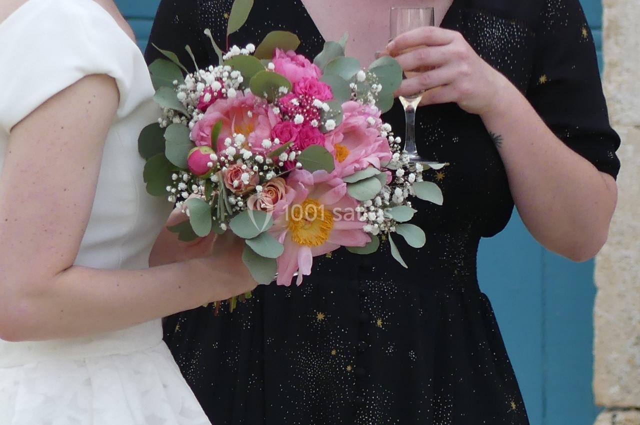 Deux femmes, l'une en robe blanche tenant un bouquet de fleurs colorées, discutent devant une porte bleue.
