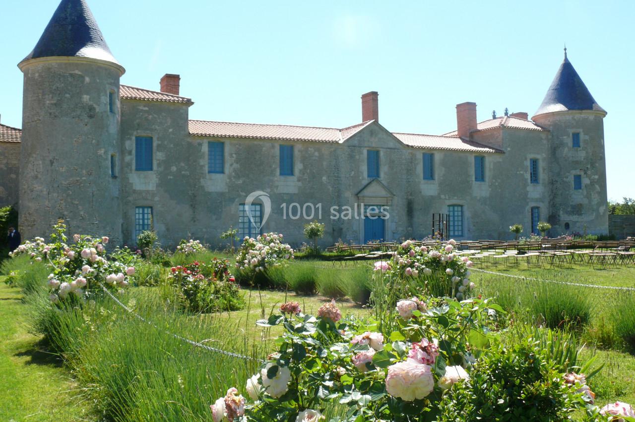 Façade d'un château en pierre avec tours, entouré d'un jardin fleuri et de pelouses bien entretenues.