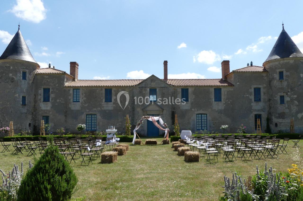 Façade d'un château en pierre avec une cérémonie en plein air, des chaises et des bottes de paille disposées sur la pelouse.